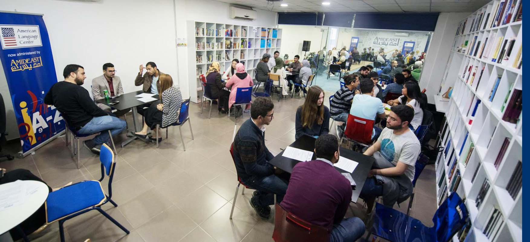 Students sit at tables while practicing their English with each other