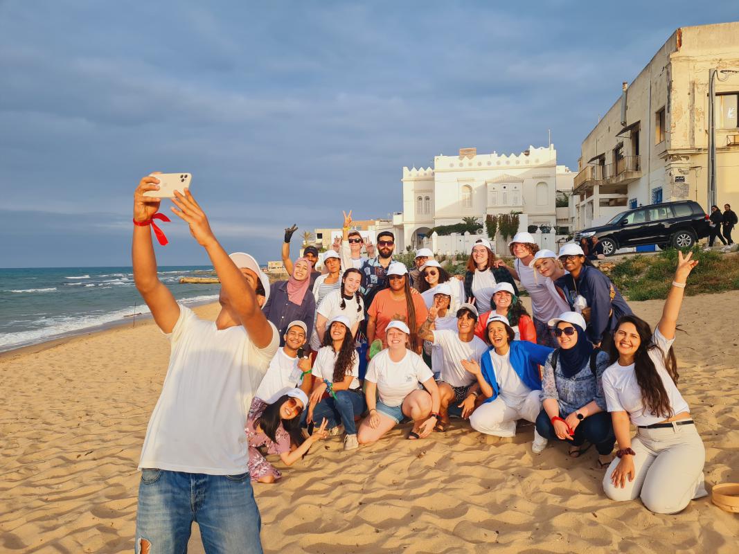 One individual takes a selfie with a group on the beach in Tangier