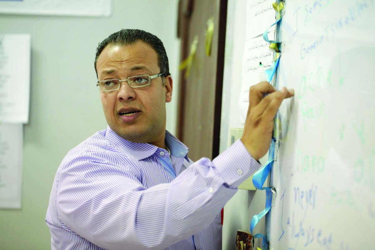 A moroccan teacher is writing something on the board while looking back and speaking to his students