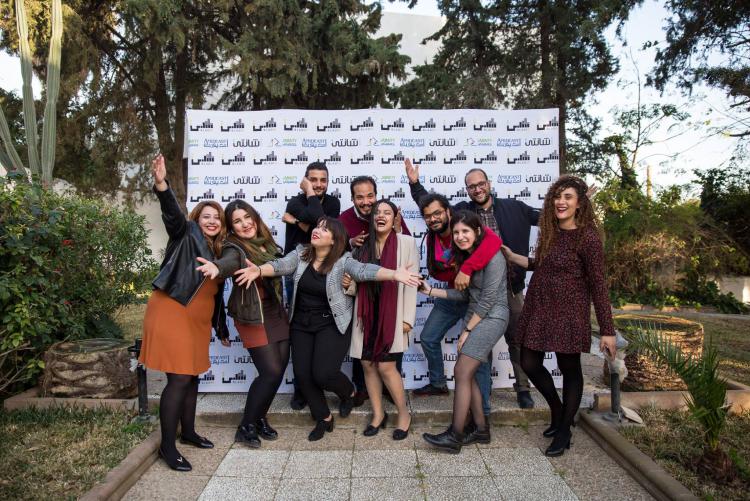 A group of BLADI participants happily pose in front of a sign with the Amideast logo on it