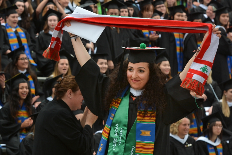 Graduating student holds up a scarf with the Lebanese flag on it at her ceremony