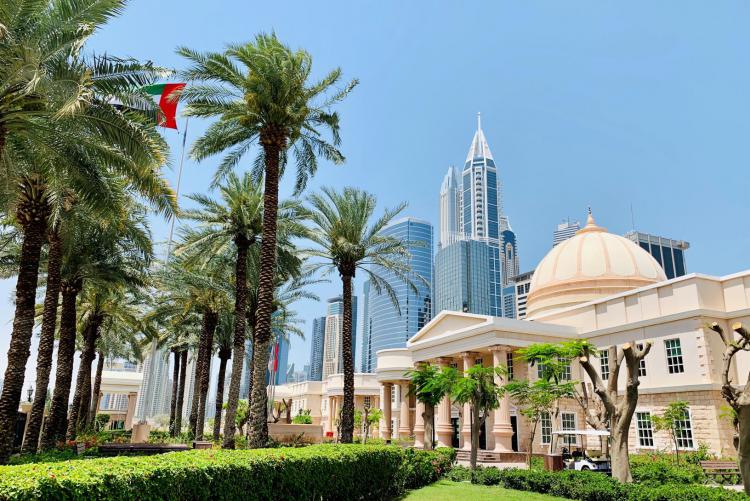 The American University in Dubai campus is in the foreground on a sunny day with palm trees. In the background you can see the skyscrapers of Dubai.