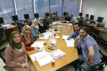 A group of graduate students sit around a table and smile at the camera, there are pens and papers in front of them