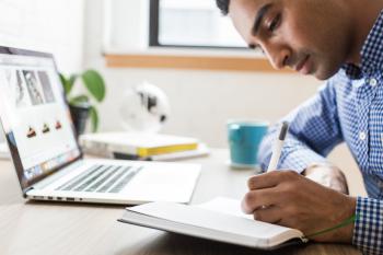 Man taking notes with laptop in the background