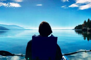 A woman faces away from the camera while sitting in a chair and looking at a lake and mountain landscape in Glacier National Park