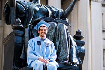 Graduating student poses on statue wearing cap and gown