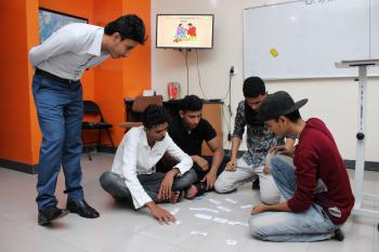 An EFL instructor is supervising a group of students who are sitting on the ground doing a jigsaw activity     y 