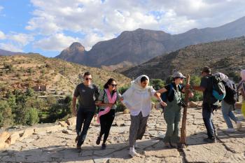 Students link arms and dance on a terrace that overlooks rolling hills that turn into mountains in the distance.