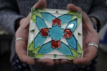 A student holds a square mosaic tile that they made