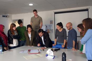 Students stand around their calligraphy teacher who is showing them how to write