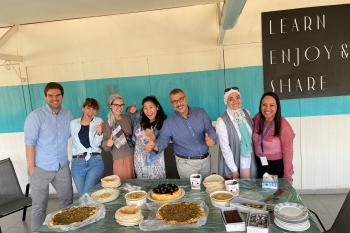 Students stand smiling with their Arabic teachers behind a table laden with many snacks and treats.