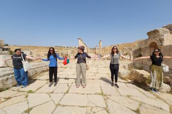 Students hold hands and smile while standing spread out across a walkway in Jerash