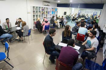 Students sit at tables while practicing their English with each other