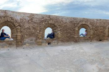 Students sit inside separate arches in a panorama image of an old wall.