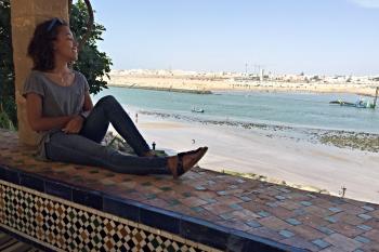 A student sits in the shade with their back to a pillar and looking out at the marina in Rabat