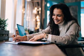 Women taking notes in a cafe with laptop behind her