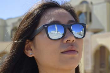 A close-up of a woman's face with sunglasses on. In the reflection of the sunglasses, you can see the famous mosque of Casablanca