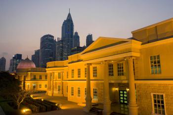 The buildings of AUD are lit up with the skyline of Dubai dark in the background. It is around dusk and the sky is beginning to get dark.