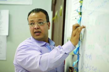 A moroccan teacher is writing something on the board while looking back and speaking to his students