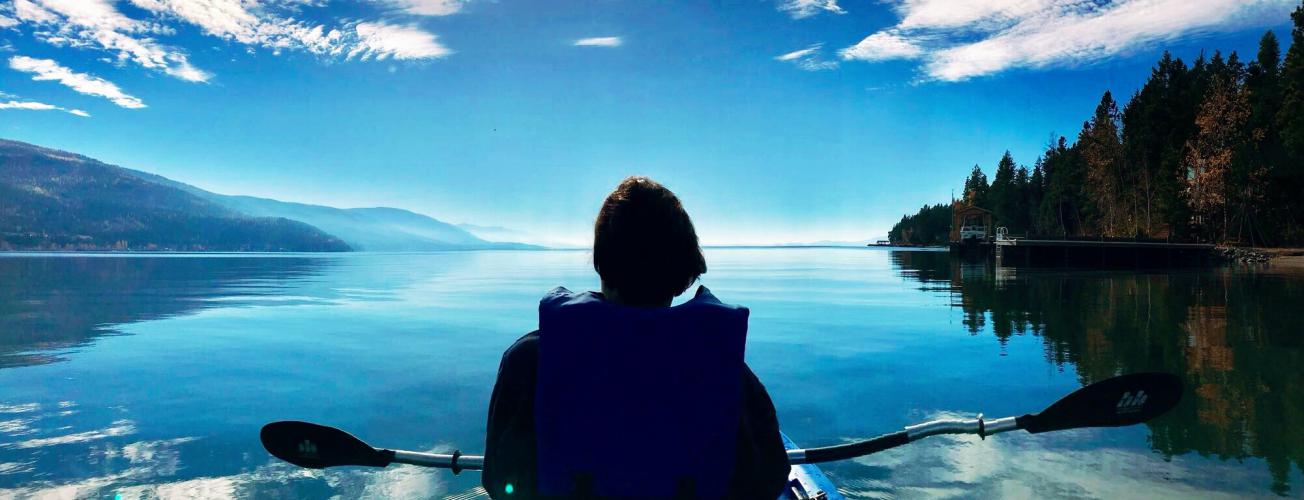 A woman faces away from the camera while sitting in a chair and looking at a lake and mountain landscape in Glacier National Park