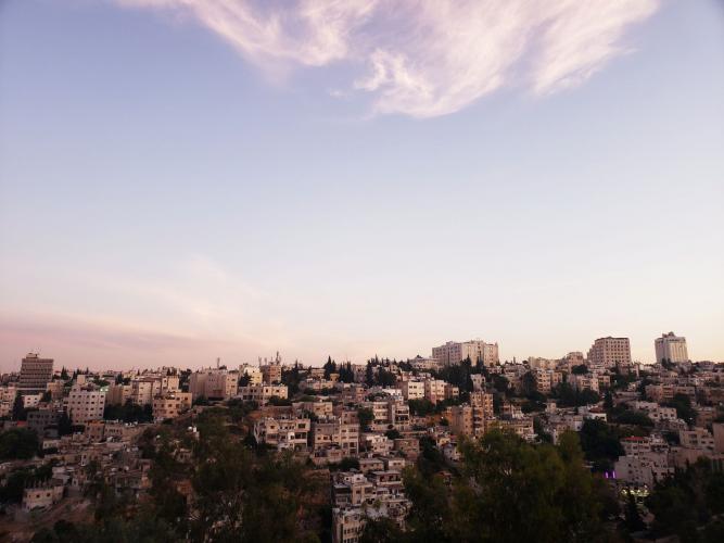 The skyline of Amman at sunset the buildings in the distance and the sky is prominent and a rosy color at the horizon but clear blue at the top.