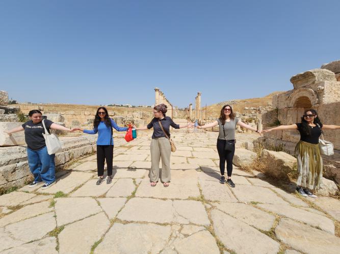 Students hold hands and smile while standing spread out across a walkway in Jerash