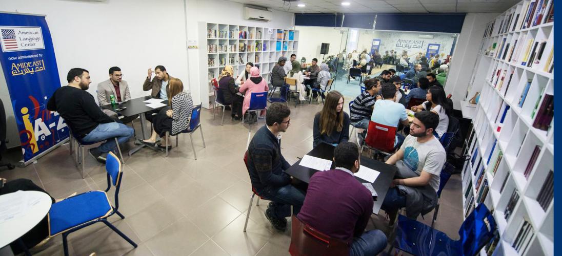 Students sit at tables while practicing their English with each other
