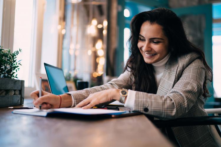 Women taking notes in a cafe with laptop behind her