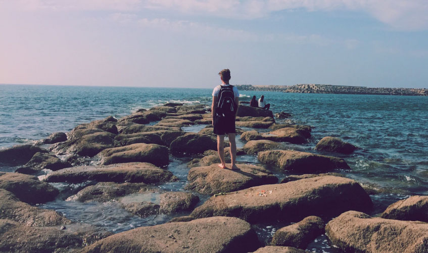 Student walks on rocks jutting into the Atlantic Ocean in Rabat, Morocco