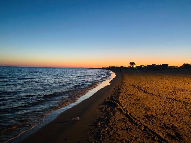 The sun sets over the beach that is on the left of the frame and the sand is on the right and there are no people