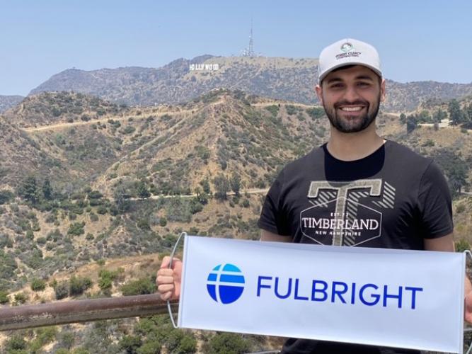 College student in front of Hollywood sign in Los Angeles holding banner with Fulbright program logo