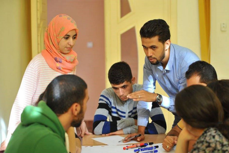 A teacher talks to students while they sit around a table