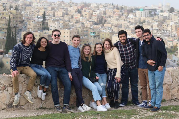 A large group of students poses together in front of a view of Amman