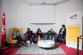 A small group of adults sits on a couch and chairs while one man speaks into a microphone