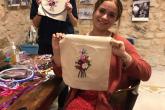 Two women hold up embroidery that they were making with flower patterns