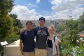 Three students pose from a vantage point where the city of Amman is in the distance.