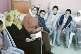 سيدتان تقرأان كتابًا لمجموعة طالبات صغيرات يرفعن أيديهن