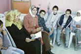 Two women read a book to a group of female students who are raising their hands