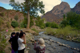 A group of women stand by the side of a stream that runs through the mountains of Morocco.