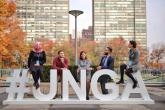 مجموعة من الطلاب يتكئون ويجلسون على لافتة الجمعية العامة للأمم المتحدة. 