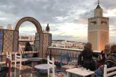 A café overlooks the old medina. A tiled archway and mosque minaret stab the sky.