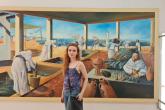 A woman stands in front of a large painting mounted in a museum