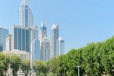 A crowd of students mills around on the green at AUD. Some students play volleyball. The skyscrapers of Dubai rise above the scene in the background