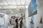 Two architecture students work on drawing boards. There are blueprints and designs on the walls and the city is visible through the windows.