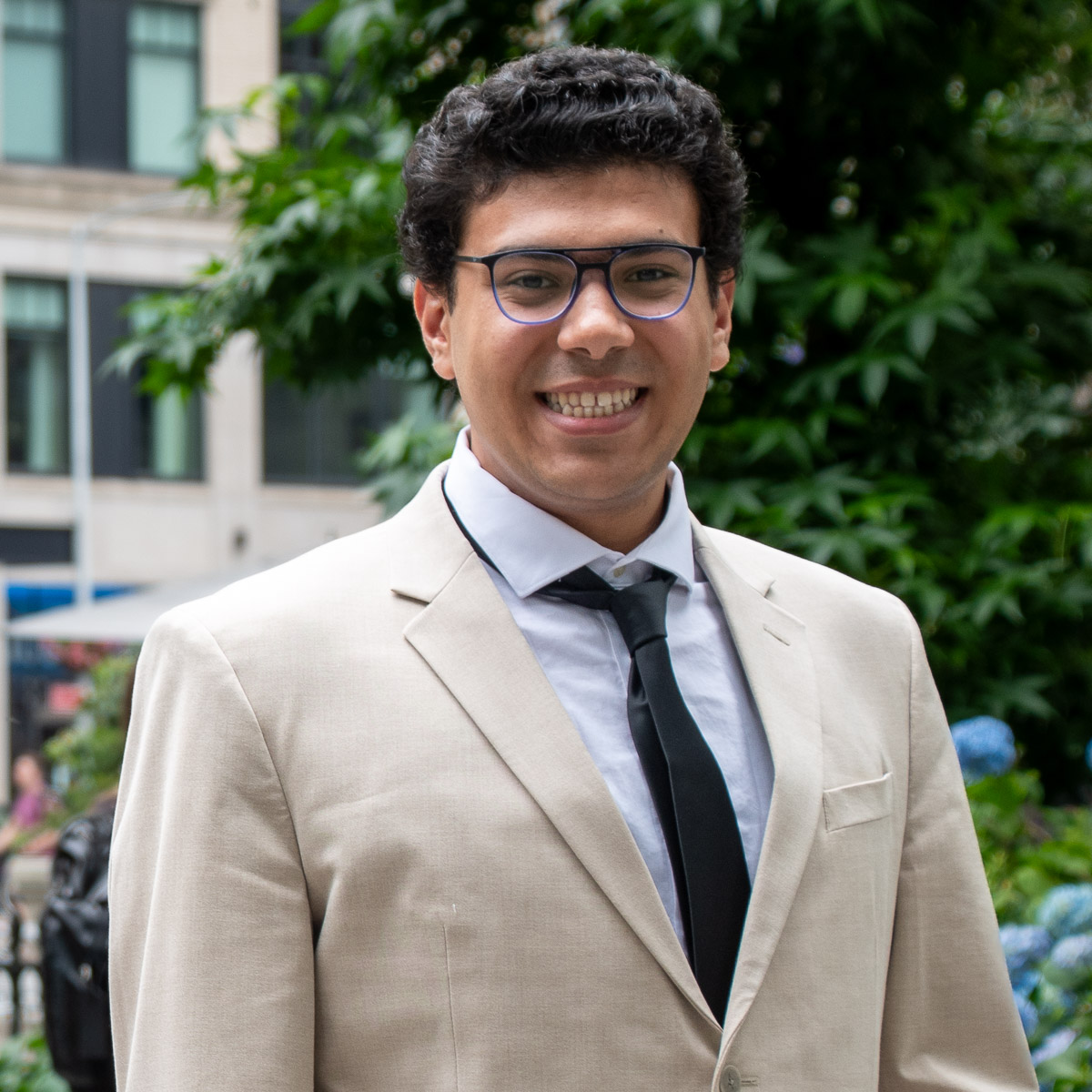 Headshot of Ahmed in a beige blazer and a navy tie