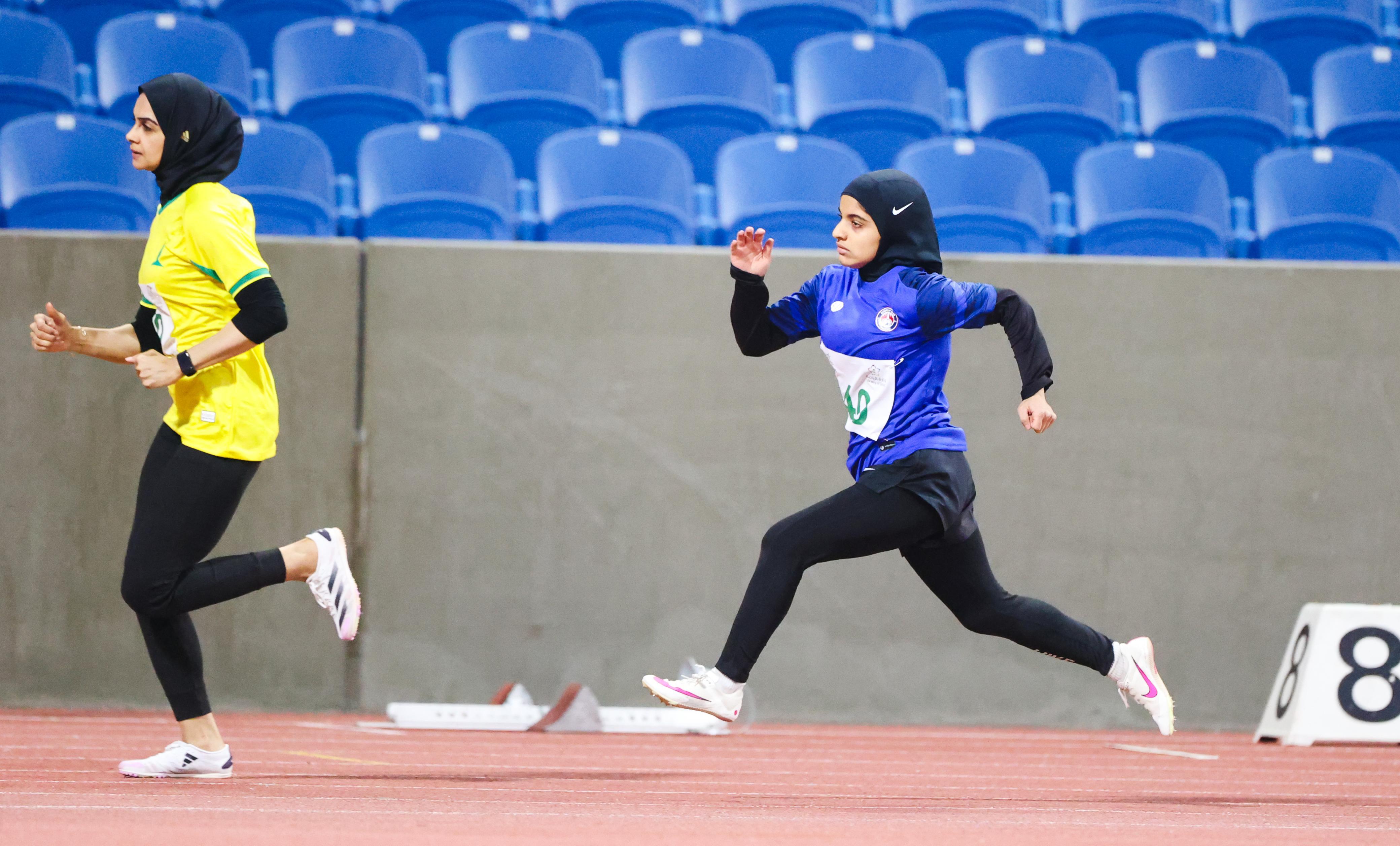 Alaa in a black hijab and blue shirt running on a track field
