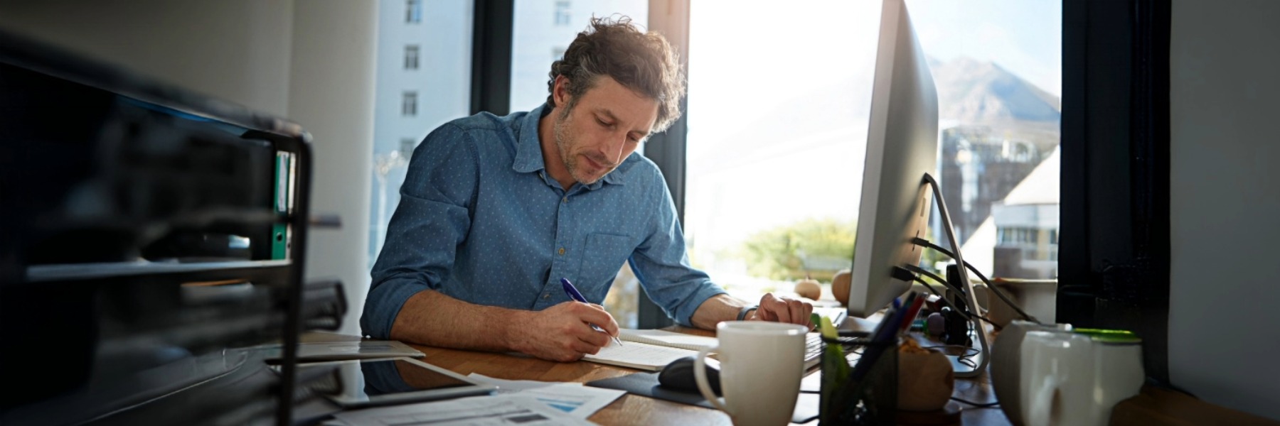 Employee writing with a pen in front of a laptop at work, focused on completing tasks in a professional office setting.
