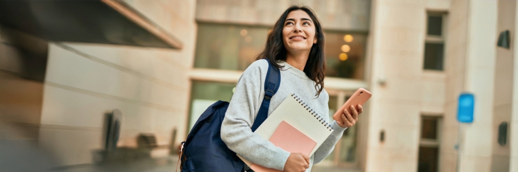 Female student smiling in front of a university building, happy and confident about her academic journey.