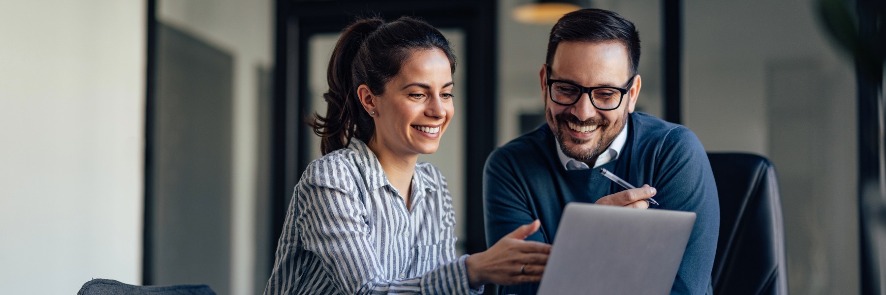 Male and female business professionals smiling and looking at a laptop