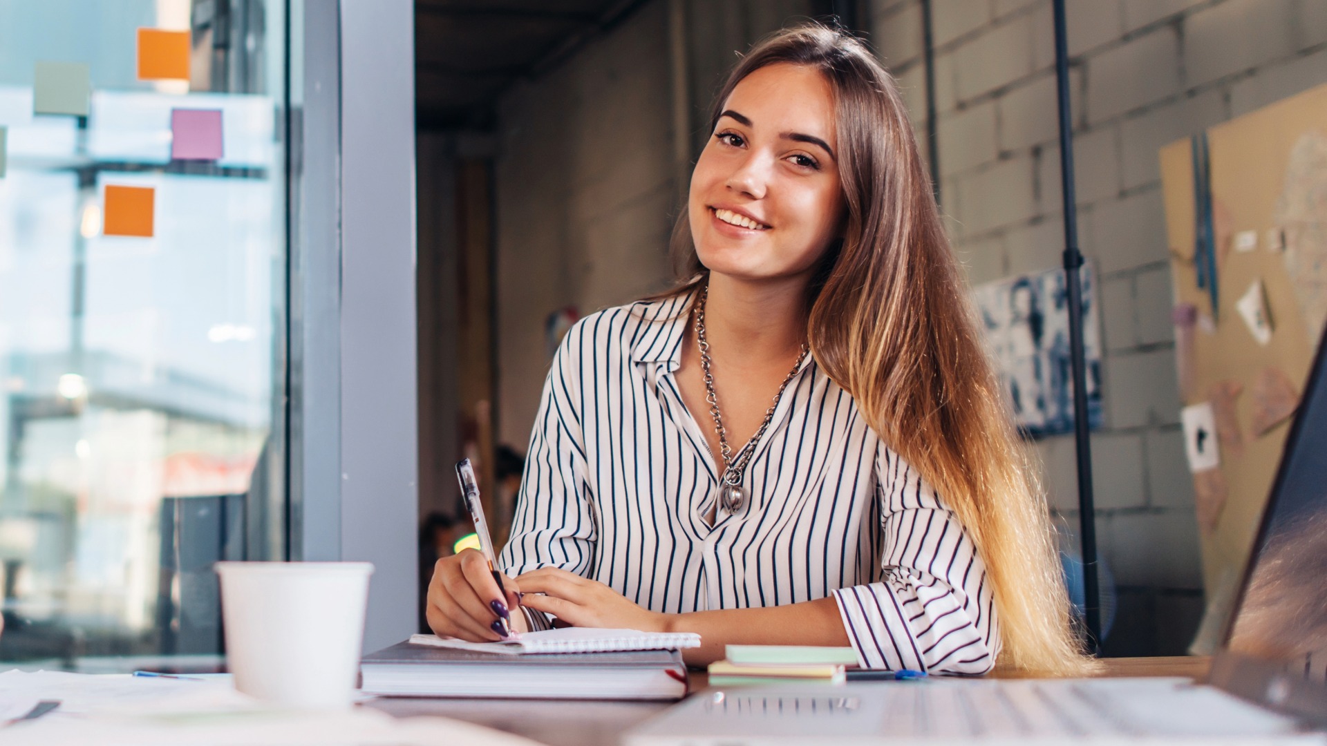 Portrait of smiling female student writing looking at camera sitting at table